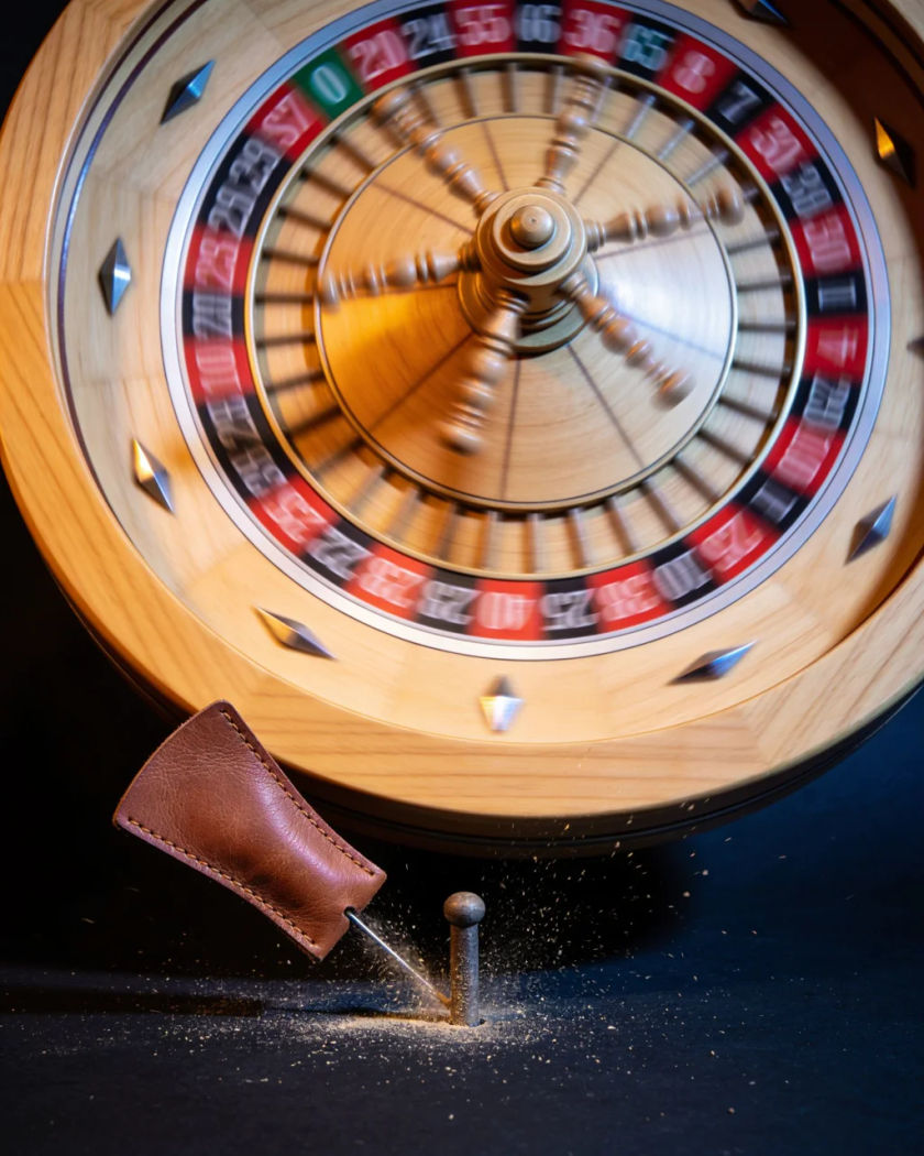 A plain prize wheel spinning in a blur, its leather flapper snapping against a peg under warm light against a dark ground