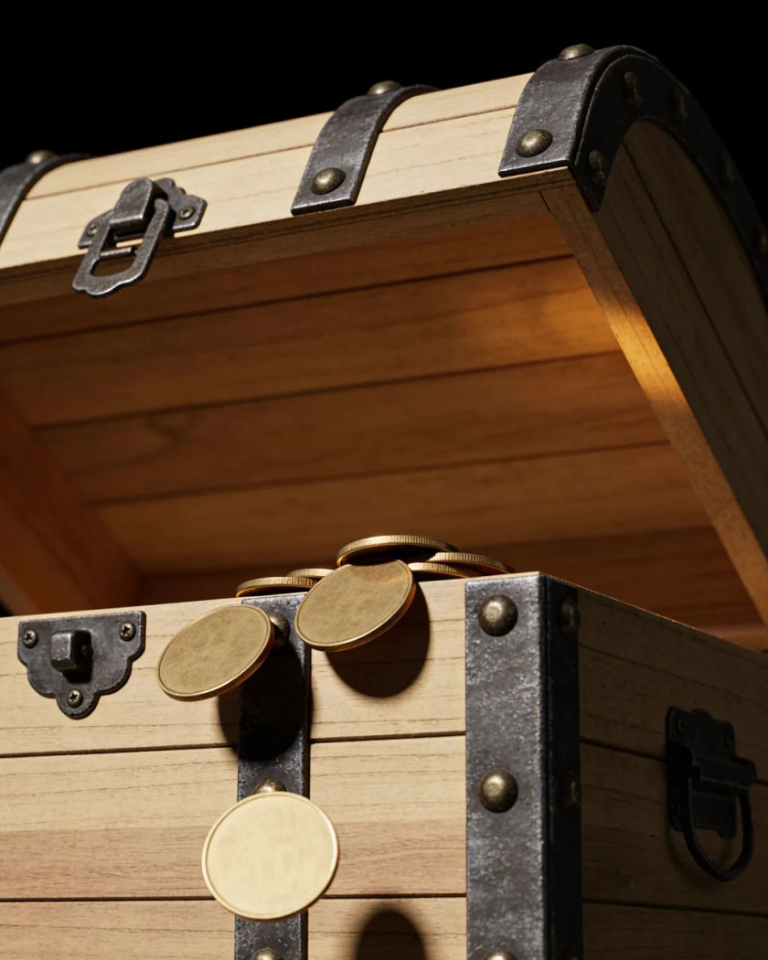 An old iron bound wooden chest with its lid half open under warm side light against a black ground, gold coins spilling over the edge