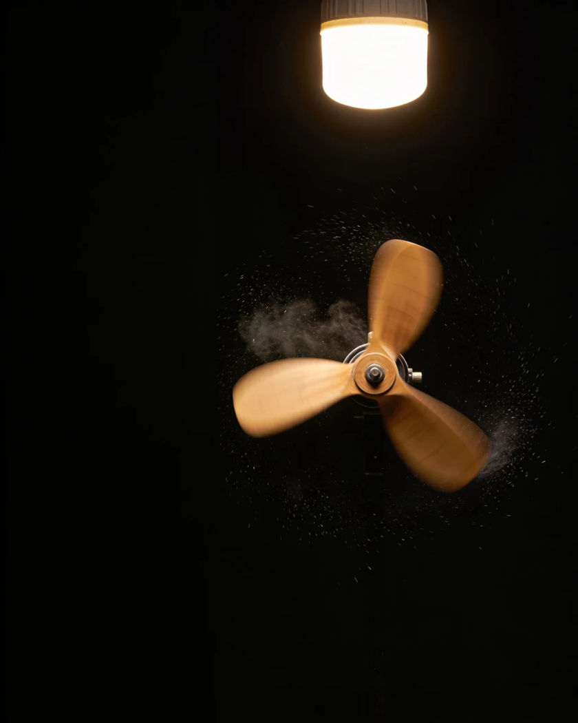A spinning aircraft propeller blurred into a disc under one warm light from above, a fine spray of mist thrown off its tips