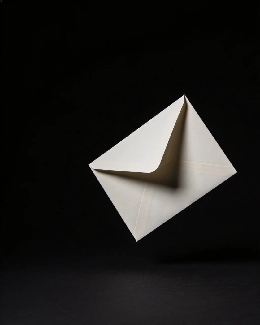 A plain folded paper envelope tumbling through warm light, its flap lifting open