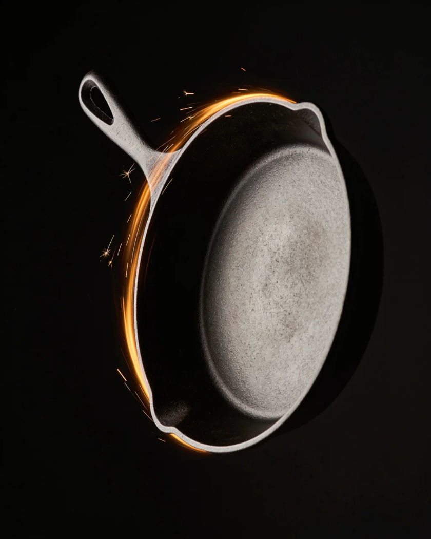 A black cast iron frying pan swinging through warm light, motion blur along its arc and light flying off its edge