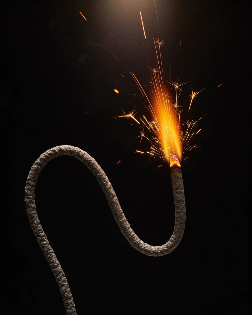 A short lit fuse seen at a low angle spraying bright sparks under warm light against a black background