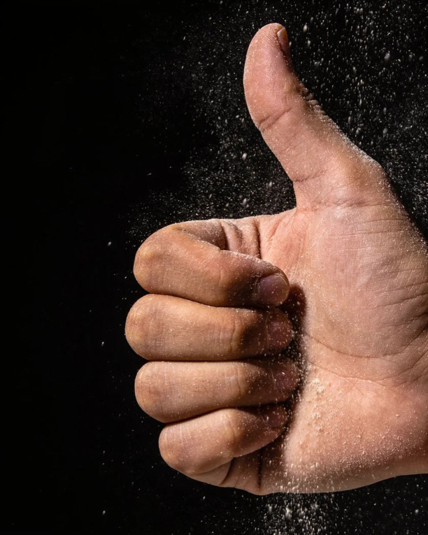 A hand raised in a firm thumbs up lit from directly above against a black background