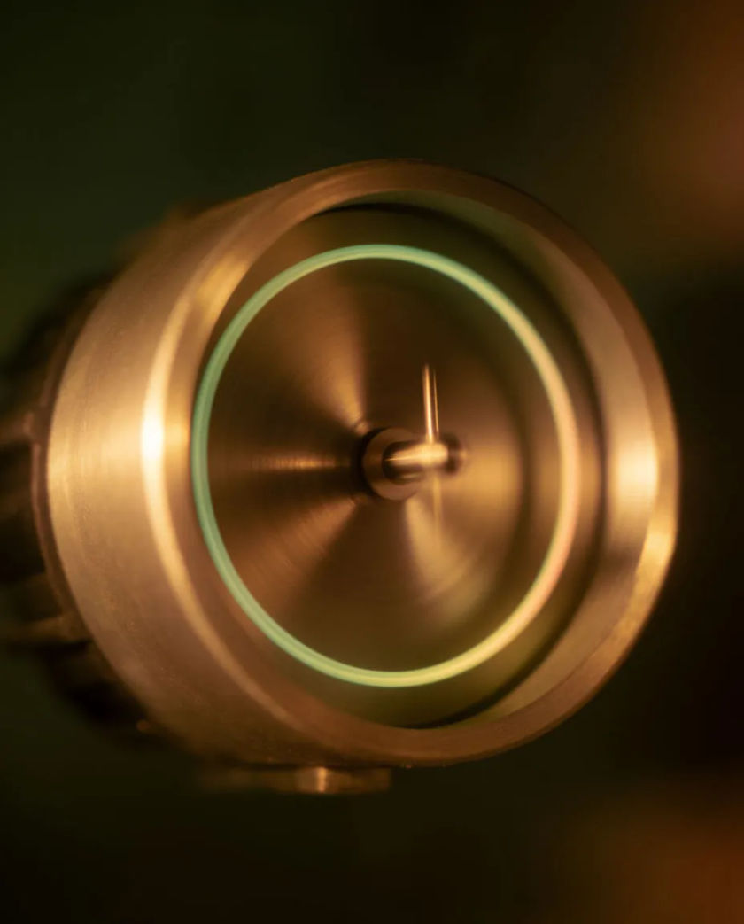 A compact motor casing with a fine metal shaft at its center, a thin halo of light tracing the spinning rotor against a black ground