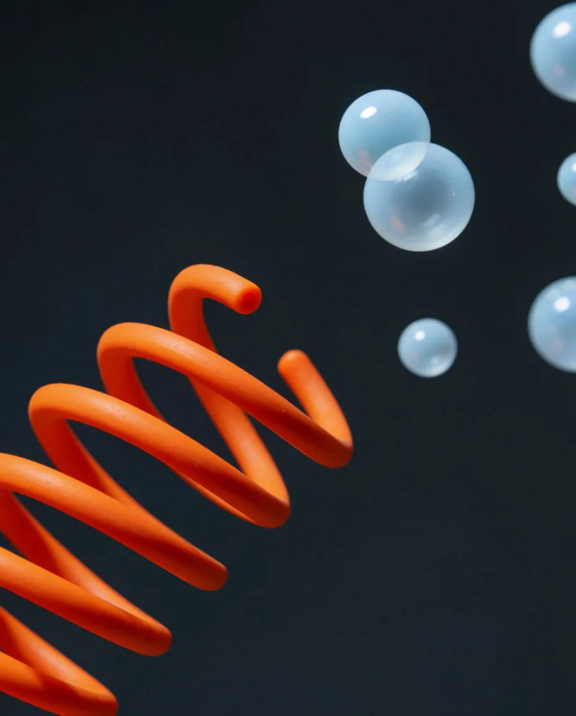 A bright rubber spring and a few soft round bubbles floating against a dark matte background, each catching a thin warm amber highlight