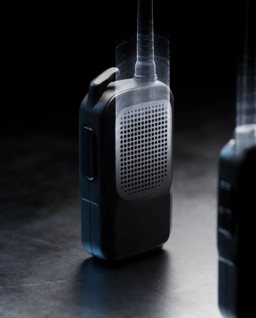 A black handheld radio on a dark steel surface, a coiled antenna and a thin band of static light rising from its speaker grille