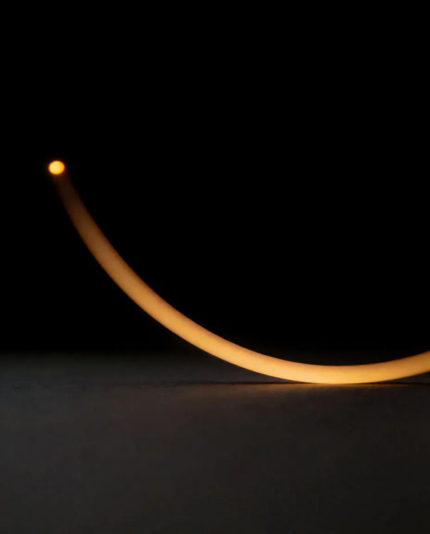 A single amber curve of light bending upward over a matte black surface and ending in a small glowing dot
