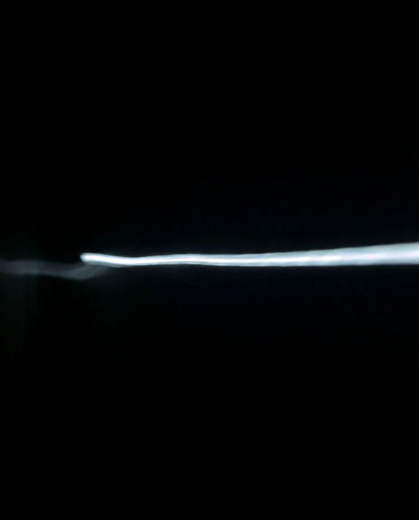 A thin streak of white light racing left to right across a black frame, a faint ghost of the same streak trailing behind it