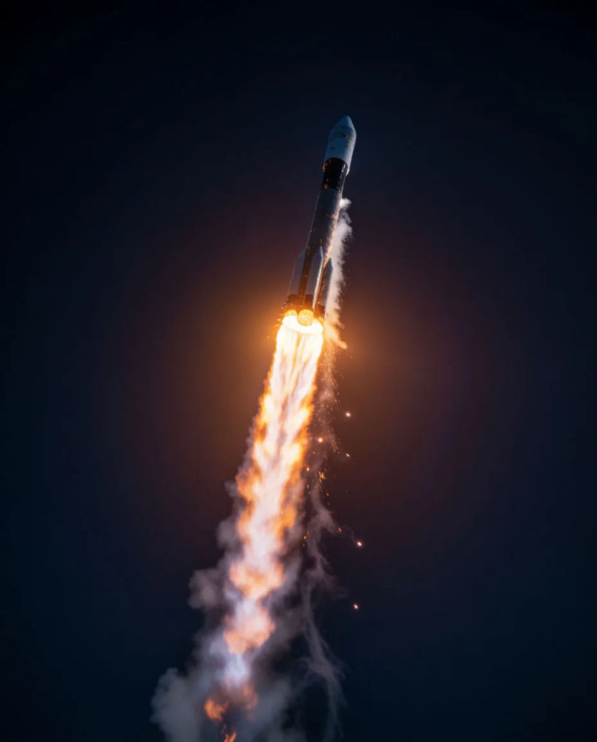 A slim metallic rocket streaking upward against a dark sky, a long tapering plume of orange fire and thin white smoke trailing below it