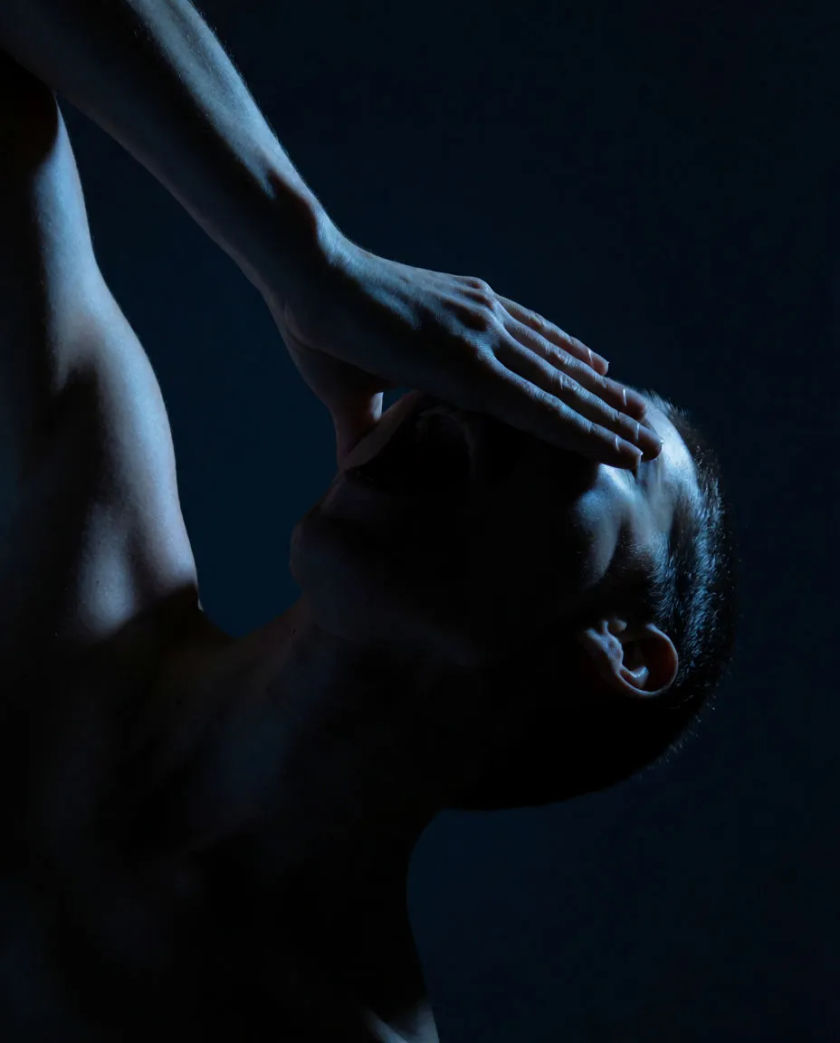 A pair of wide open eyes lit by one cold blue light from the side, the rest of the face lost in black shadow