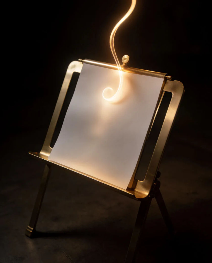 A small brass music stand holding a blank sheet on a dark stage floor, a thin ribbon of warm light curling upward from the paper