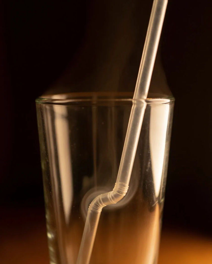 A clear drinking straw bent into an empty glass on a dark counter, a thin swirl of water vapor curling at the bottom