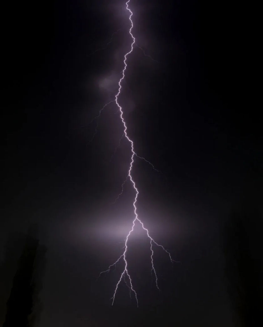 A single branching fork of pale violet light splitting a black frame from top to bottom, with a faint glow haze around its base