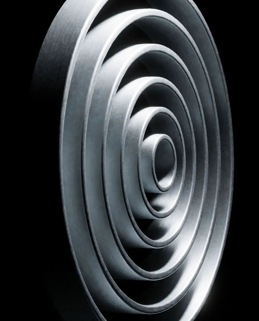Concentric rings of brushed steel stacking upward into a narrowing spiral on a matte black ground, a thin line of cold white light along each edge