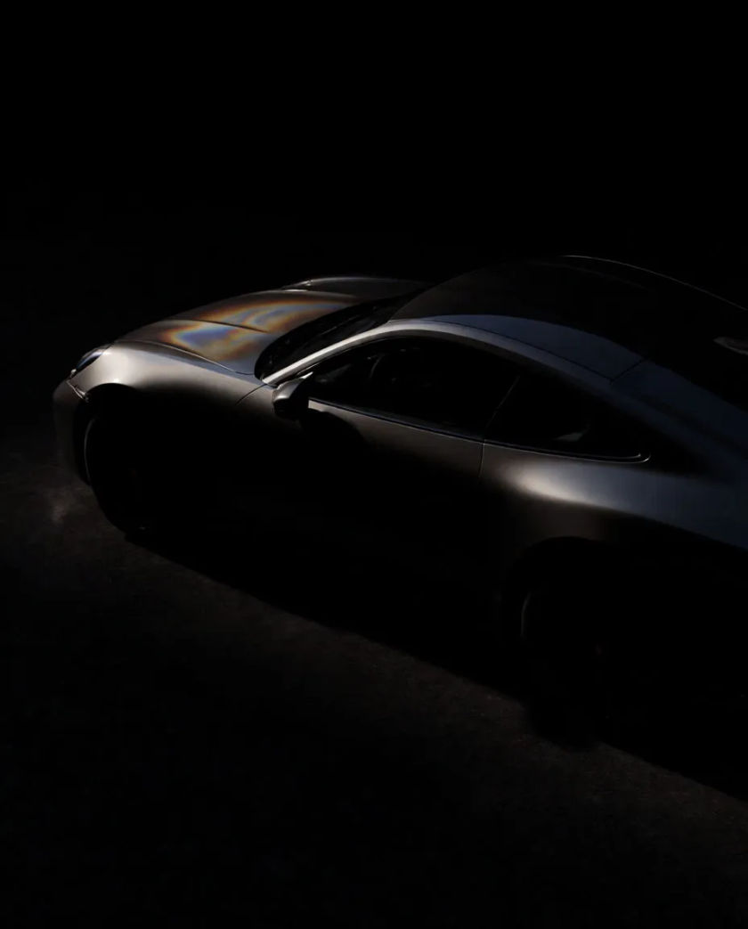A low sleek unmarked sports car in dark metallic paint, a thin line of light along its flank and a faint heat shimmer, near-black ground