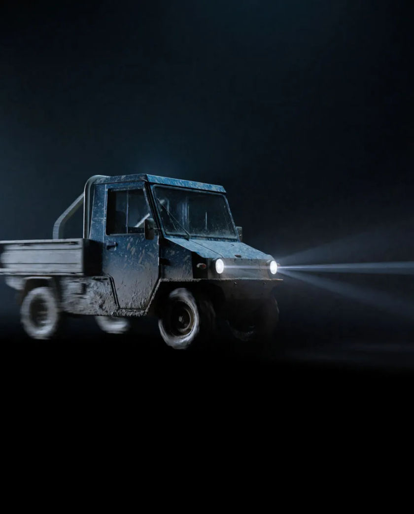 A small mud-streaked work vehicle with a flat cargo bed caught side-on mid-turn, its headlamps cutting two thin beams through haze against black