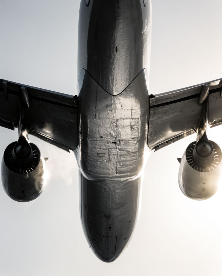The underside of a wide-body jet filling the frame low overhead, heat rippling off the engines against pale sky