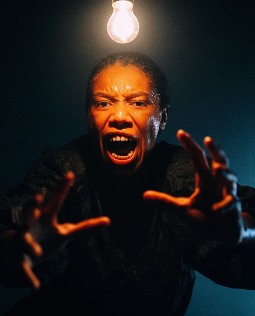 A figure lunging out of deep shadow into one hard beam of light, mouth open mid-shout