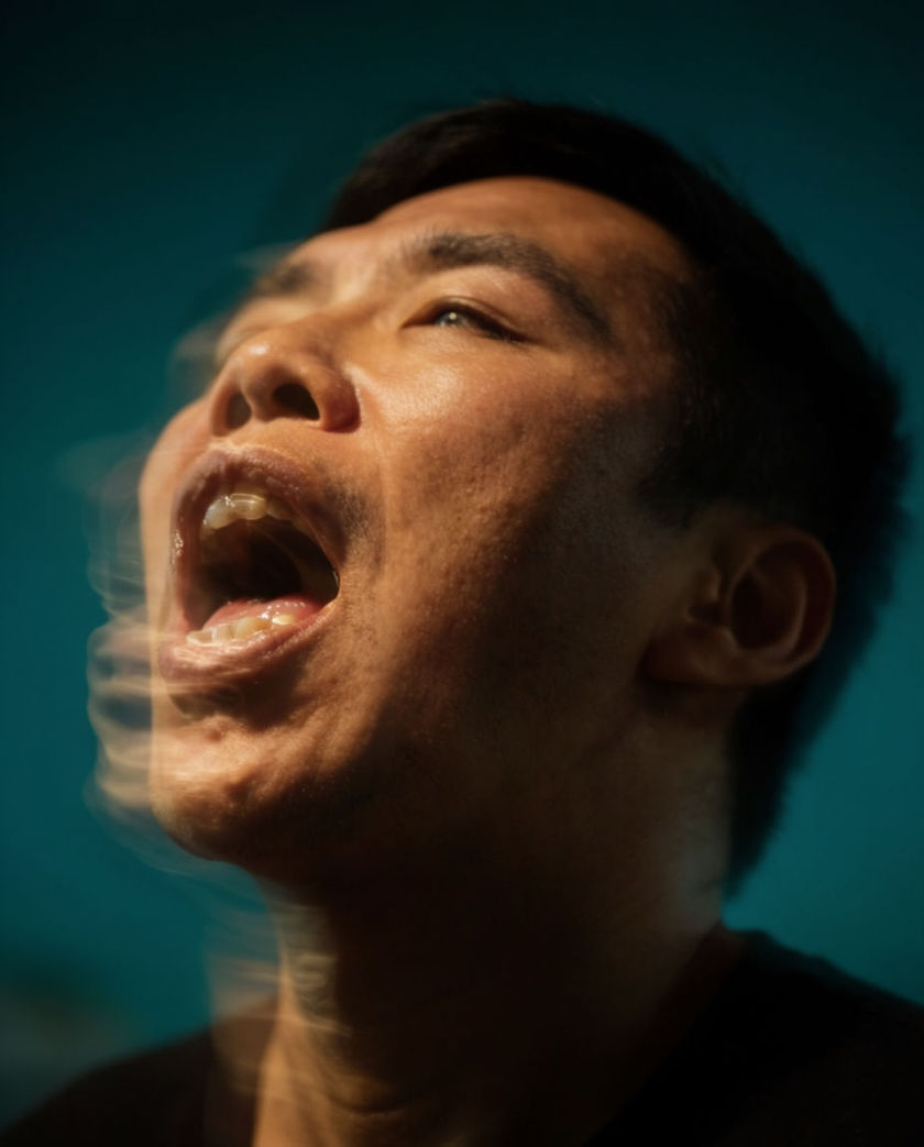 A close frame on an open mouth caught mid-release, air distorting the light across the lower lip