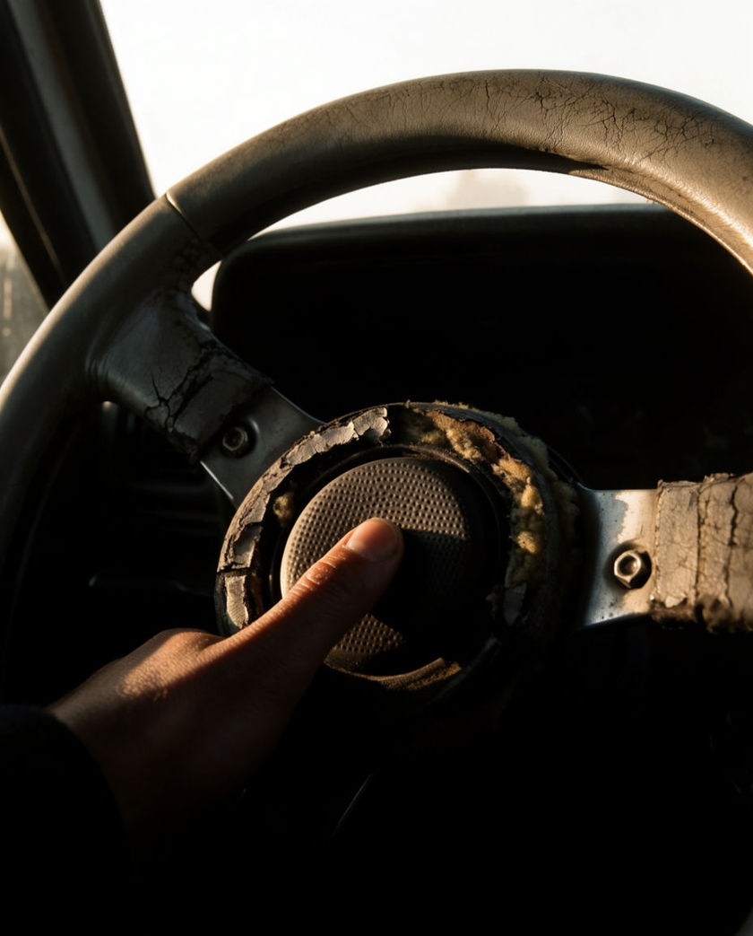 A close view of a worn steering wheel boss with a thumb pressing into it, the windscreen beyond it blown out to white