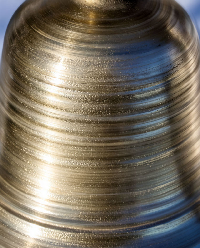 A small brass bell dome struck mid-ring, concentric rings of light rippling off its curve against deep shadow