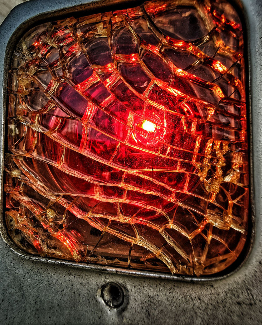 A red indicator lamp behind cracked glass filling most of the frame, its glow bleeding across the fractures