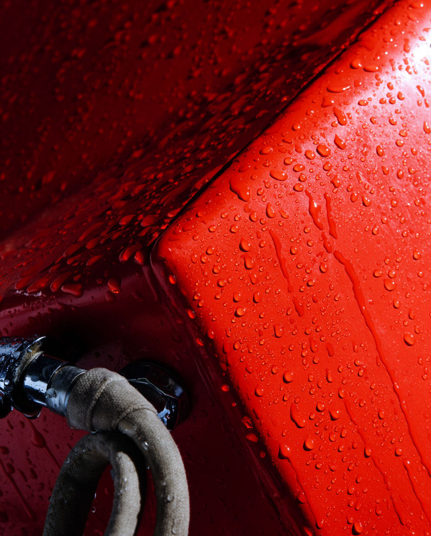 A red appliance panel filling the frame with chrome fittings and coiled hose, hard light raking across the wet metal