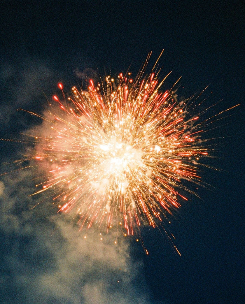 A shell caught at the instant of bursting, sparks flung outward across the whole frame in gold and red