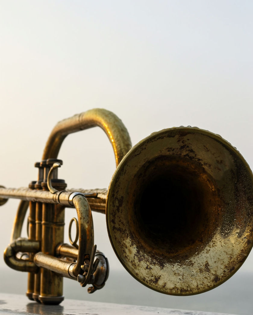 A weathered brass horn trumpet on a light station gallery, its mouth filling the frame against pale grey air