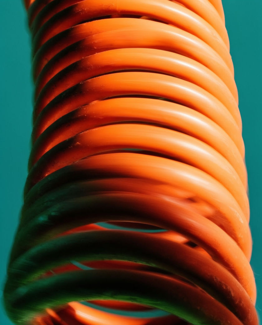 A bright rubbery coil spring caught mid-stretch against a bold flat colour, its curve blurred by speed
