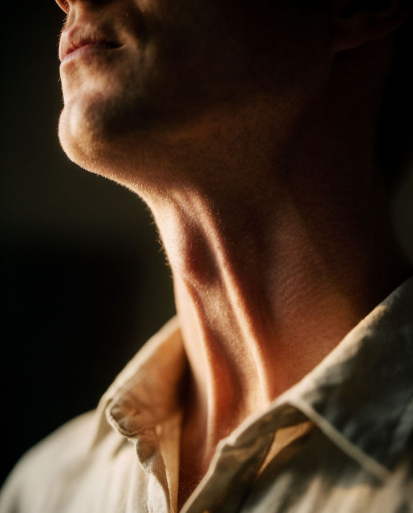 A throat in three-quarter profile filling the frame, the tendon drawn tight mid-swallow under raking side light