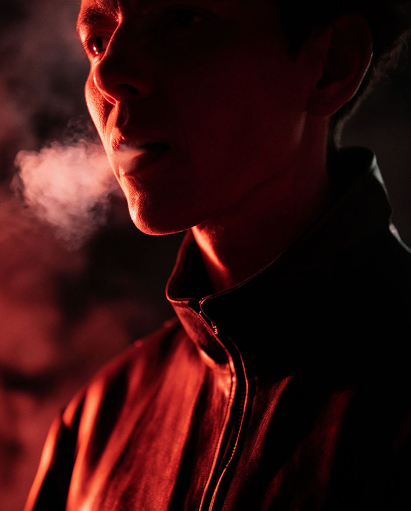 A close 4:5 frame of an open mouth and throat mid-breath, skin catching one hard raking light against near-black