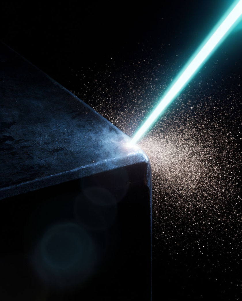 A single hard cyan beam cutting across deep blackness, striking a metal edge and throwing fine sparks outward