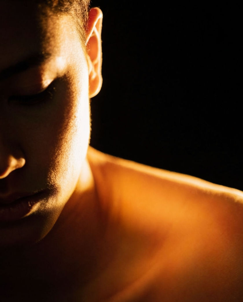 A shoulder and half a face already turning out of frame under one hard light, the rest going dark