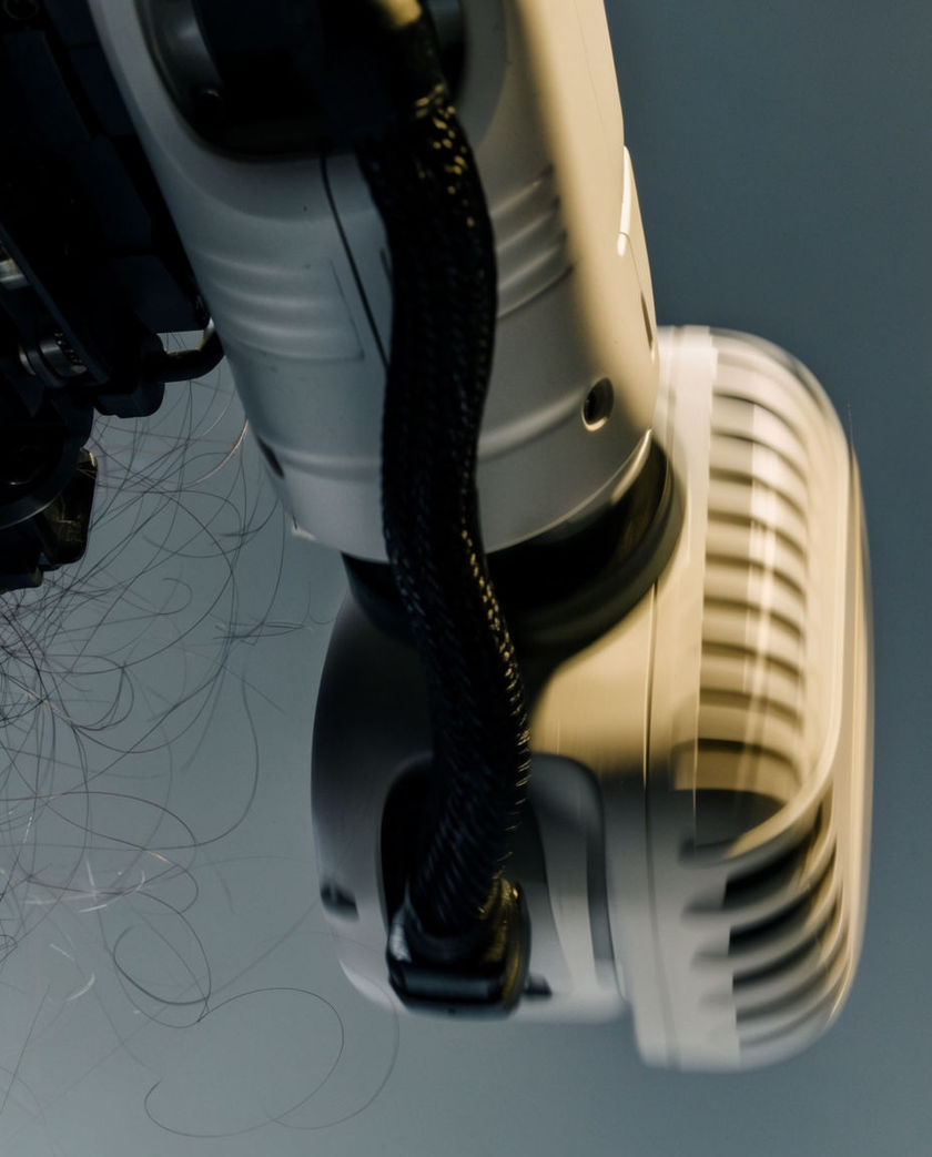 A close crop of a matte white robotic arm joint mid-rotation, cable loom and servo housing catching one hard edge of light