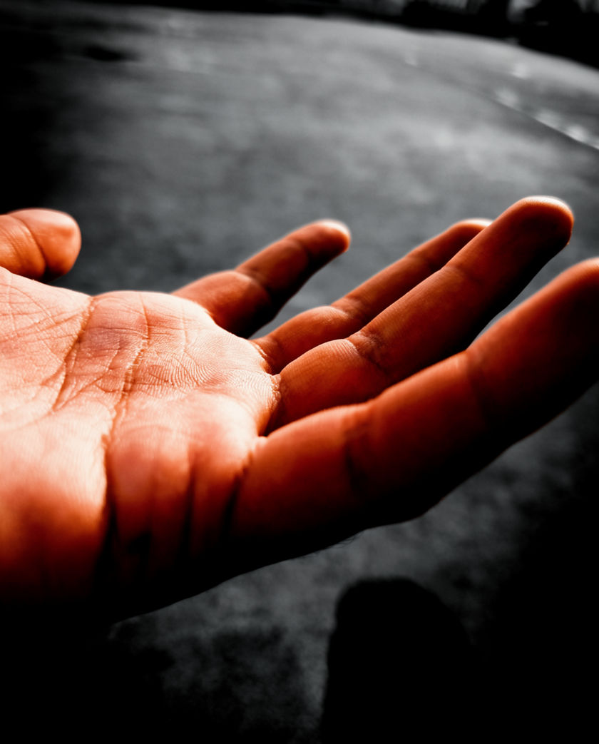 An open palm caught a frame before contact, fingers spread, hard side light and deep shadow behind