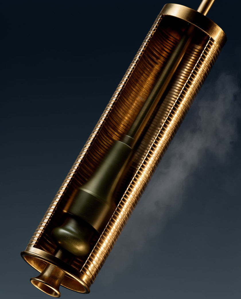 A brass slide whistle held mid-pull against a flat warm backdrop, the plunger caught in motion inside the polished tube
