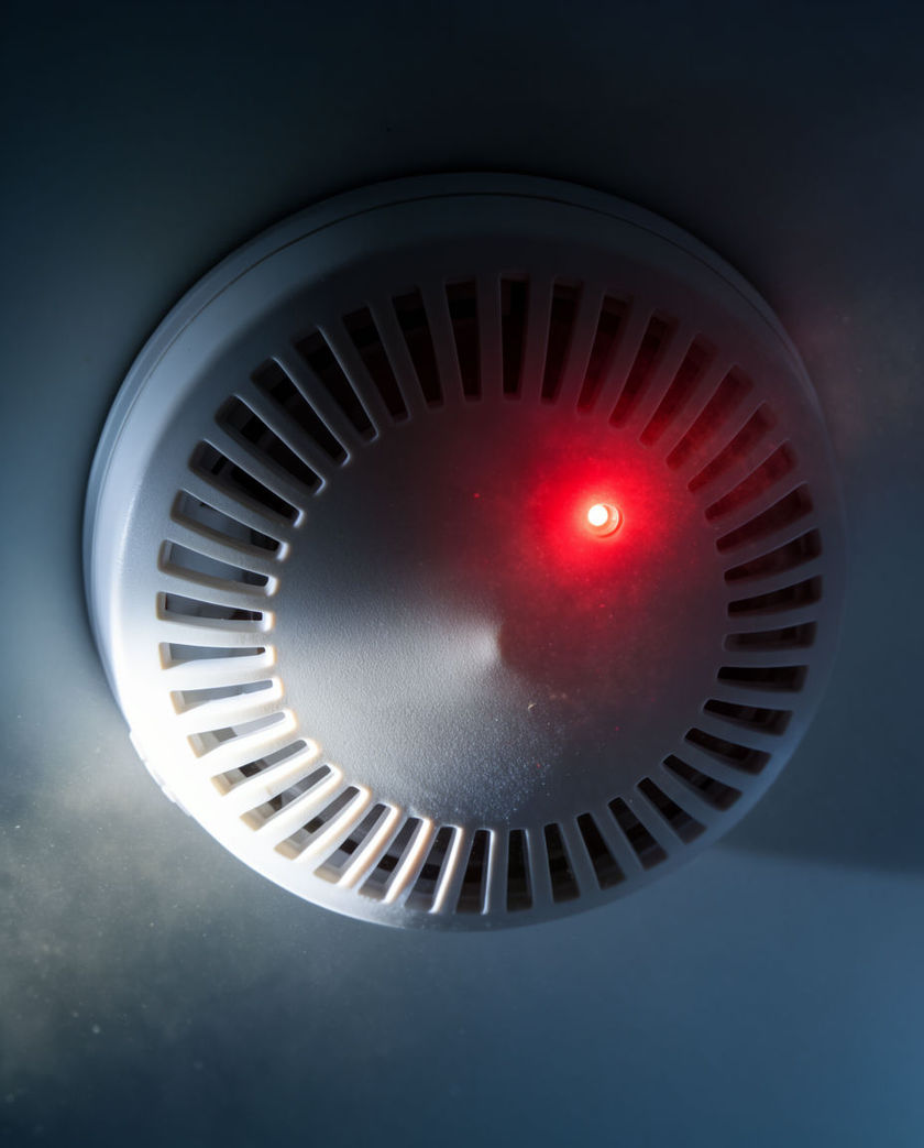 A white plastic detector disc seen from directly below, one red pinpoint lit against flat shadow