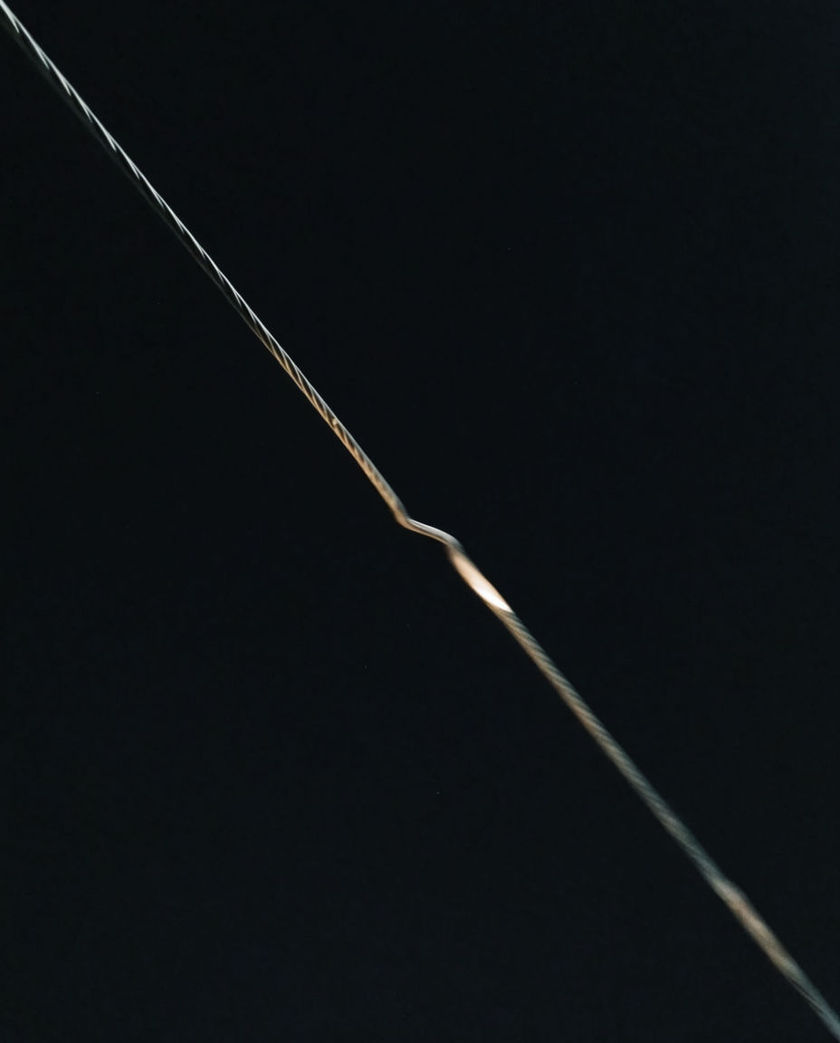 A single taut steel wire crossing a black field, one bead of hard light caught where it bends