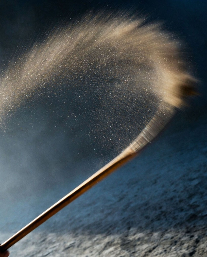 A thin cane whipping through a shaft of hard light, the air behind it smeared into a curved streak of drifting dust