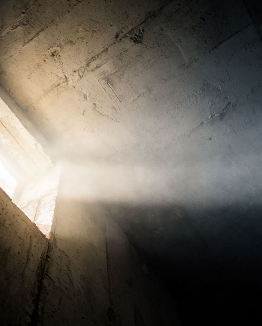 A desaturated frame draining to grey at the edges, one low shaft of light collapsing inward toward the centre