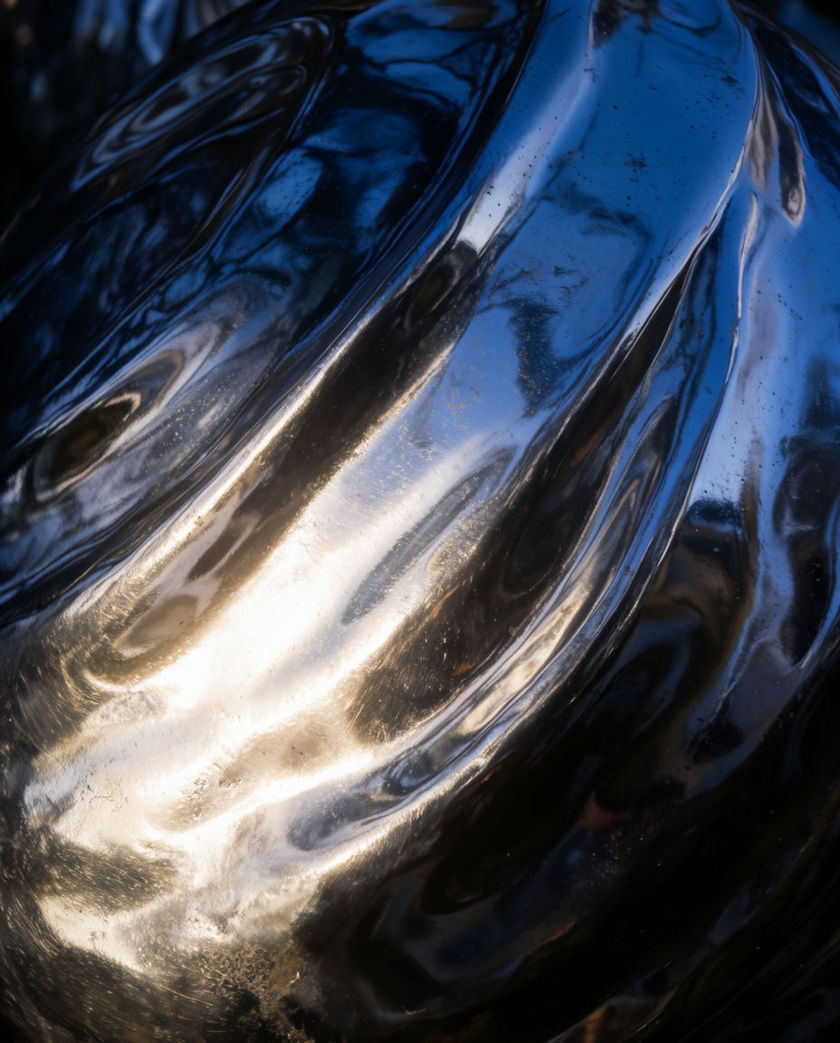 A warped sheet of thin metal rippling in strong raking light, its reflections smeared into unreadable shapes