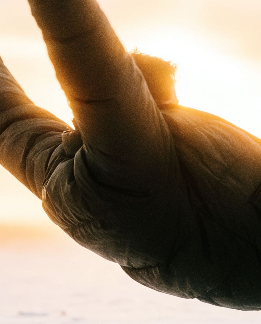 A silhouetted figure caught mid-fall against a blown-out sky, arms thrown back, edges going to grain