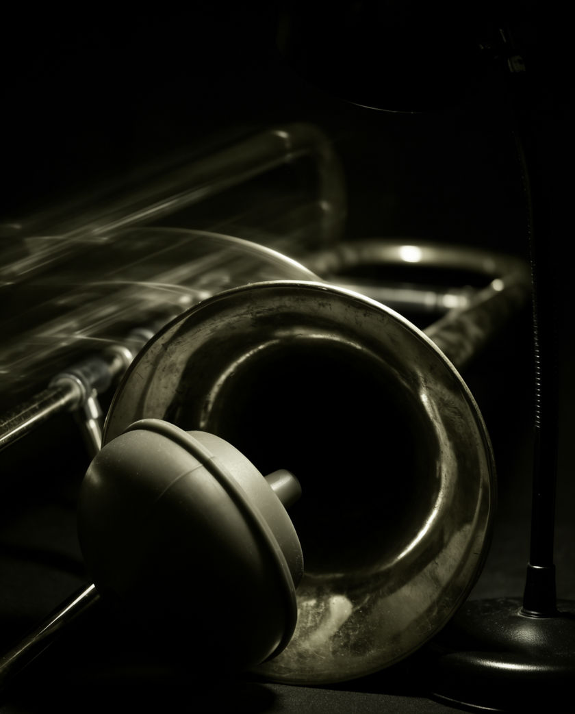 A muted trombone bell in hard side light, the slide caught mid-travel against a dark ground