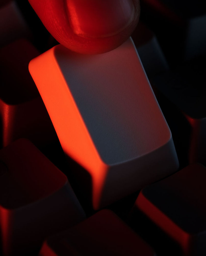 A single red-lit key on a dark keyboard caught mid-press, the surrounding keys falling away unlit