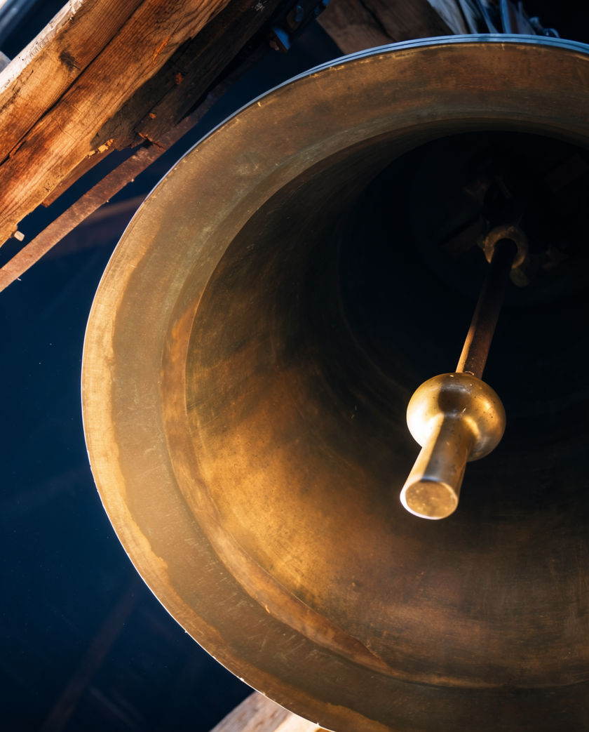 A large bronze bell in a stone tower, low light raking across the lip and the wear marks