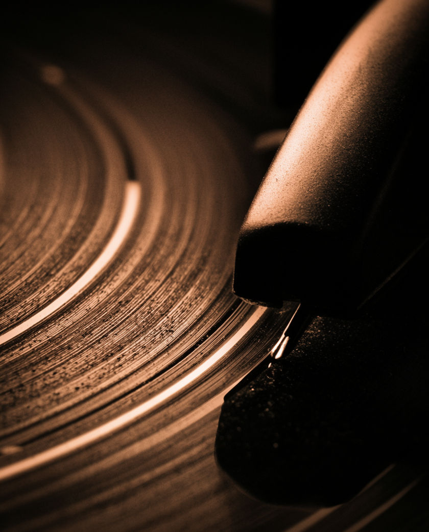 A tonearm skidding across a spinning black record, dust catching the light along the groove