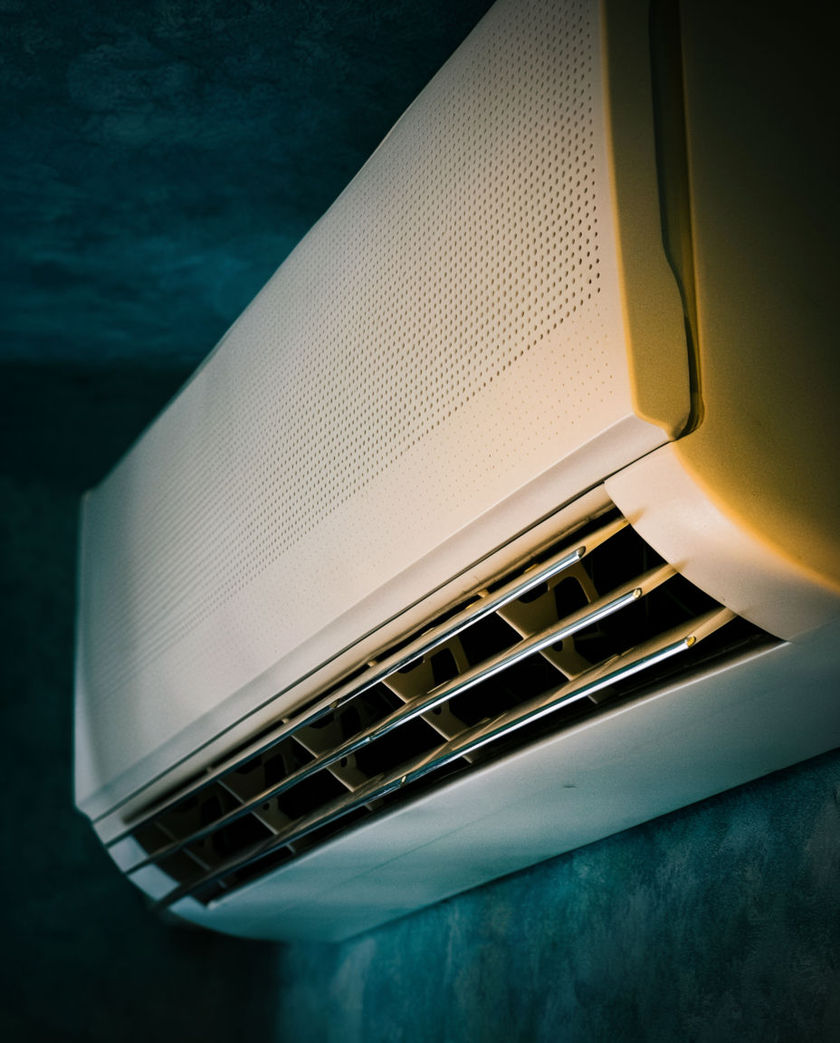 A window air conditioning unit set into a wall with its vents catching warm low side light against a dark ground