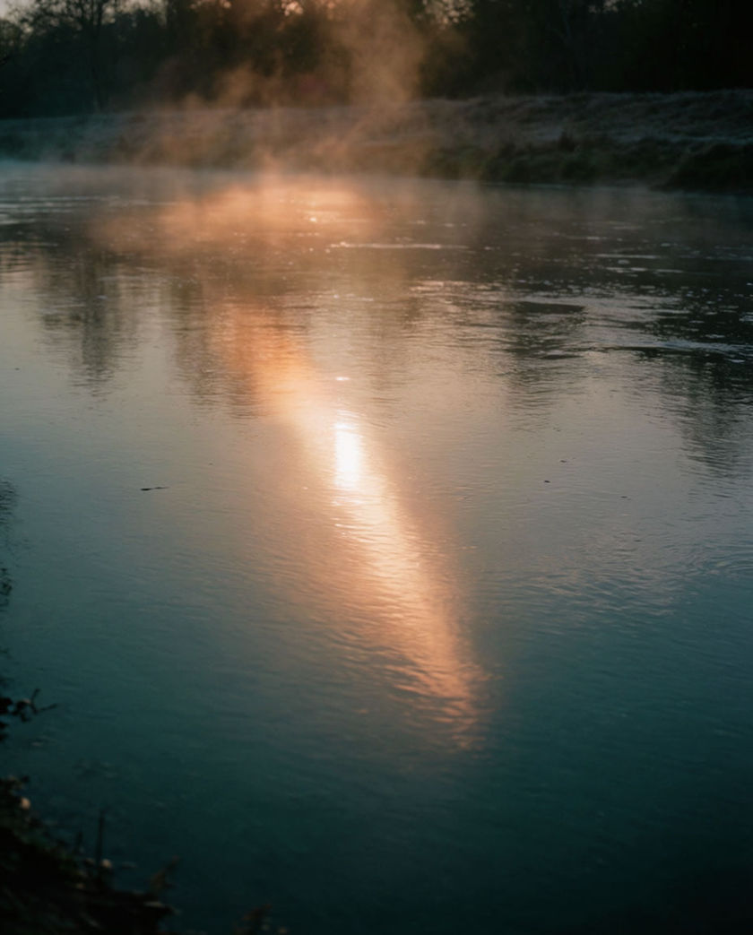 Water rushing over a single mossy rock mid-flow under warm low light against a dark bank, spray catching the light where the current breaks