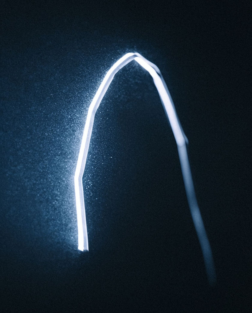 A clock face smeared into a spiral of motion blur under one warm side light against a dark ground, hands streaking